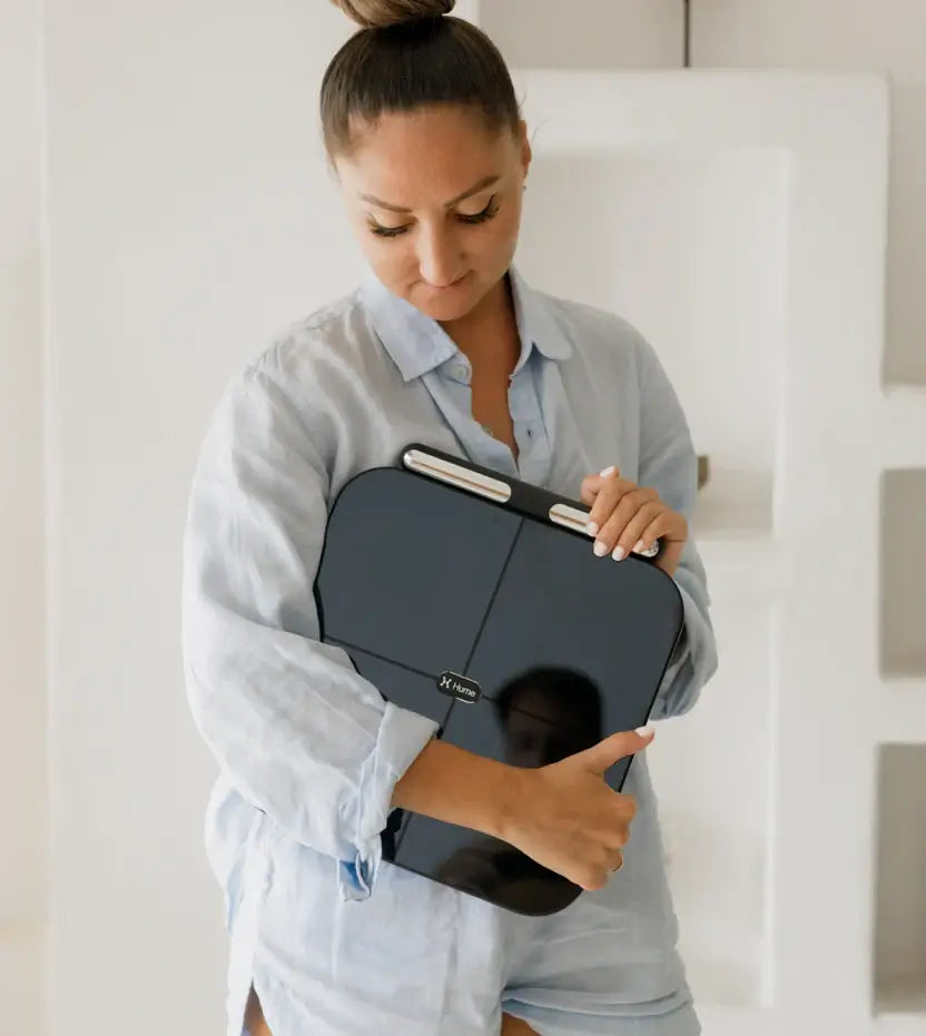 Woman holding a Hume Pod scale in her arms, showcasing a sleek smart body composition device for tracking weight, body fat, and muscle mass.